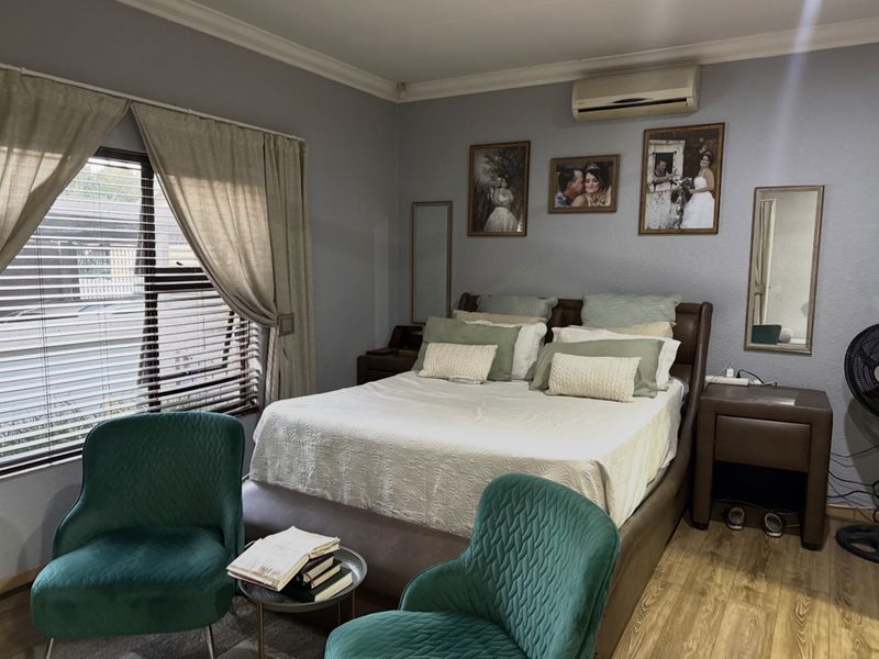 A well-maintained bedroom featuring laminate flooring, crown molding, and a wall-mounted split-system air conditioner.