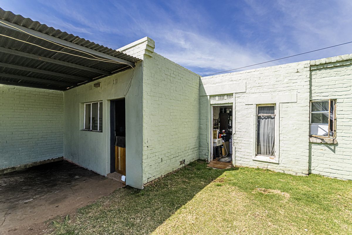 Rear exterior view of the property featuring painted brick walls, a covered patio area, and steel-framed windows.