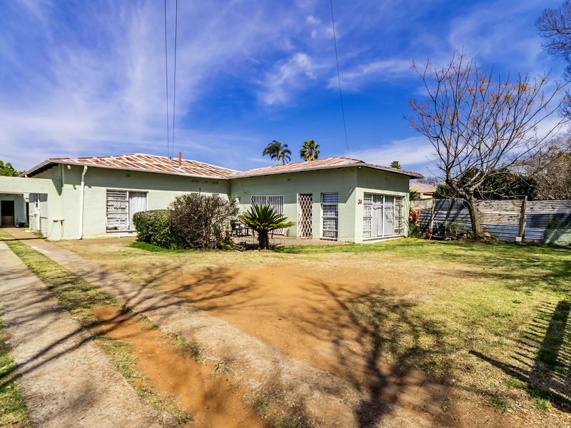 Rear view of a single-story house featuring a corrugated metal roof, concrete driveway, and sliding glass doors opening onto a large backyard area.