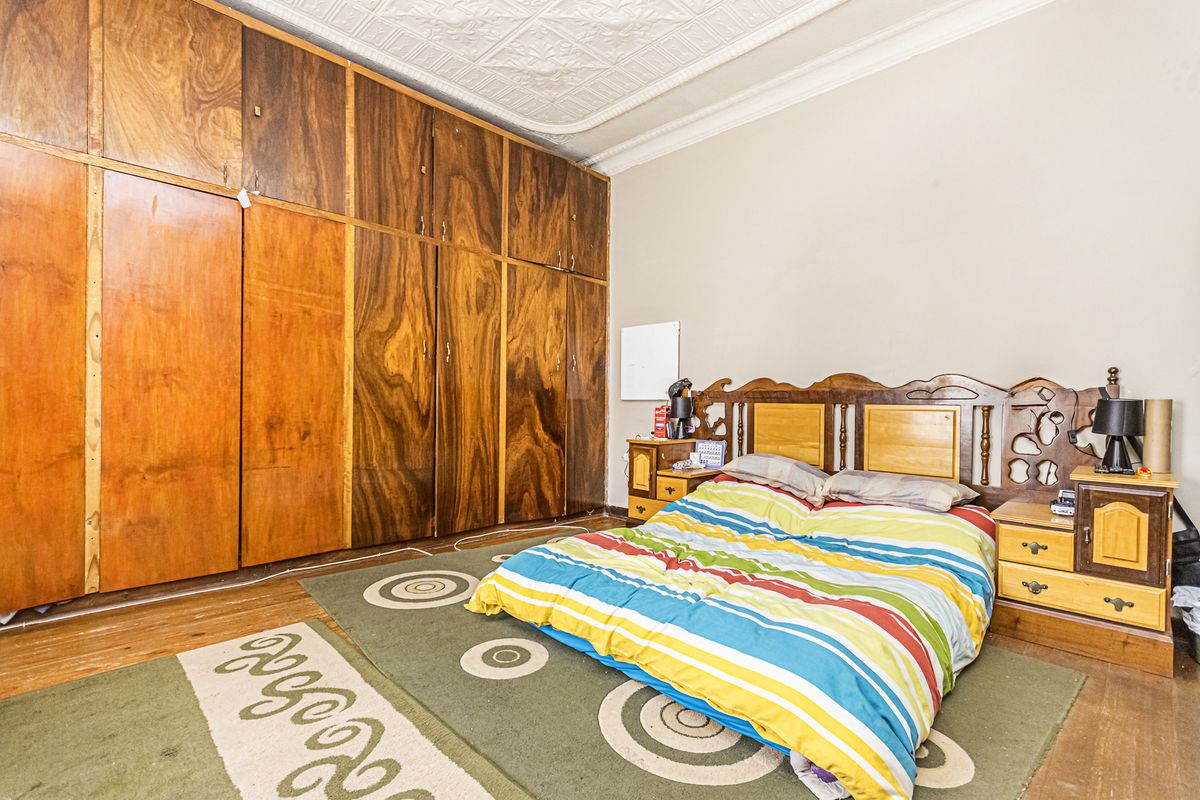 Spacious bedroom featuring extensive built-in wooden cabinetry, classic pressed metal ceiling detailing, and original timber flooring.