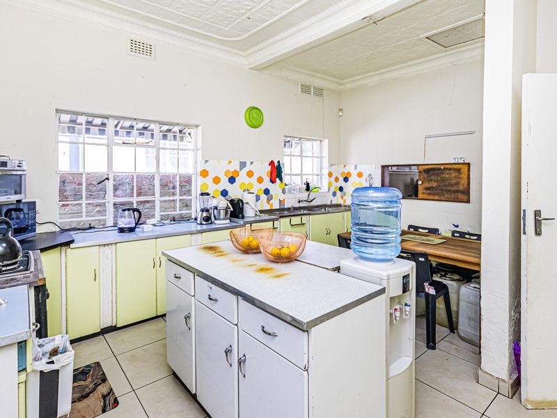 A dated kitchen featuring original cabinetry, a central island, tiled splashbacks, and a classic pressed metal ceiling, offering significant potential for a modern renovation.