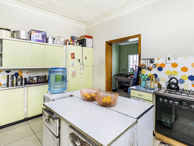A dated kitchen featuring original cabinetry, a gas stove, hexagonal tile backsplash, and a classic pressed metal ceiling, offering significant potential for renovation.