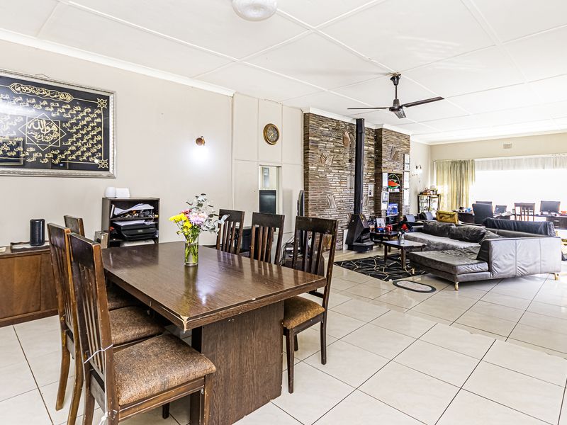 Spacious open-plan living and dining area featuring tiled floors, a prominent stone-clad fireplace with a wood-burning stove, and large windows for natural light.