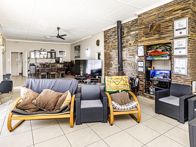 Open-plan living area featuring tiled flooring, a prominent stone-clad fireplace with a freestanding unit, and a ceiling fan.