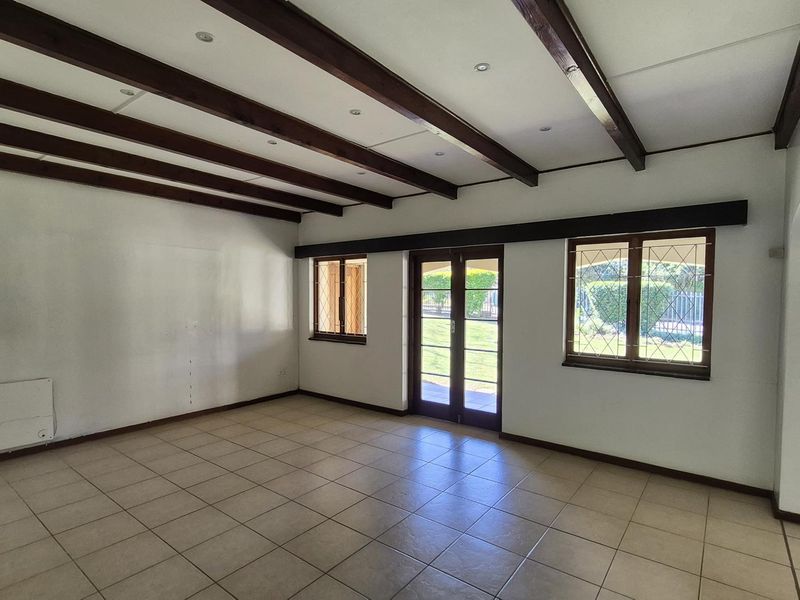Spacious living room featuring exposed timber ceiling beams, tiled flooring, and direct access to the garden through glass-paned french doors.