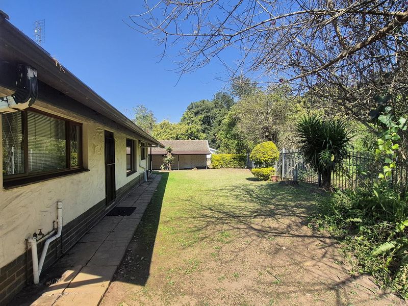 A view of the rear exterior of the house featuring a paved walkway, lawn area, and perimeter security fencing.