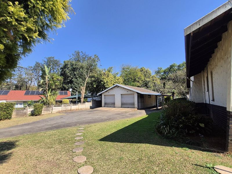 Rear view of the property featuring a double garage, paved driveway, and established garden area with brick boundary walling.