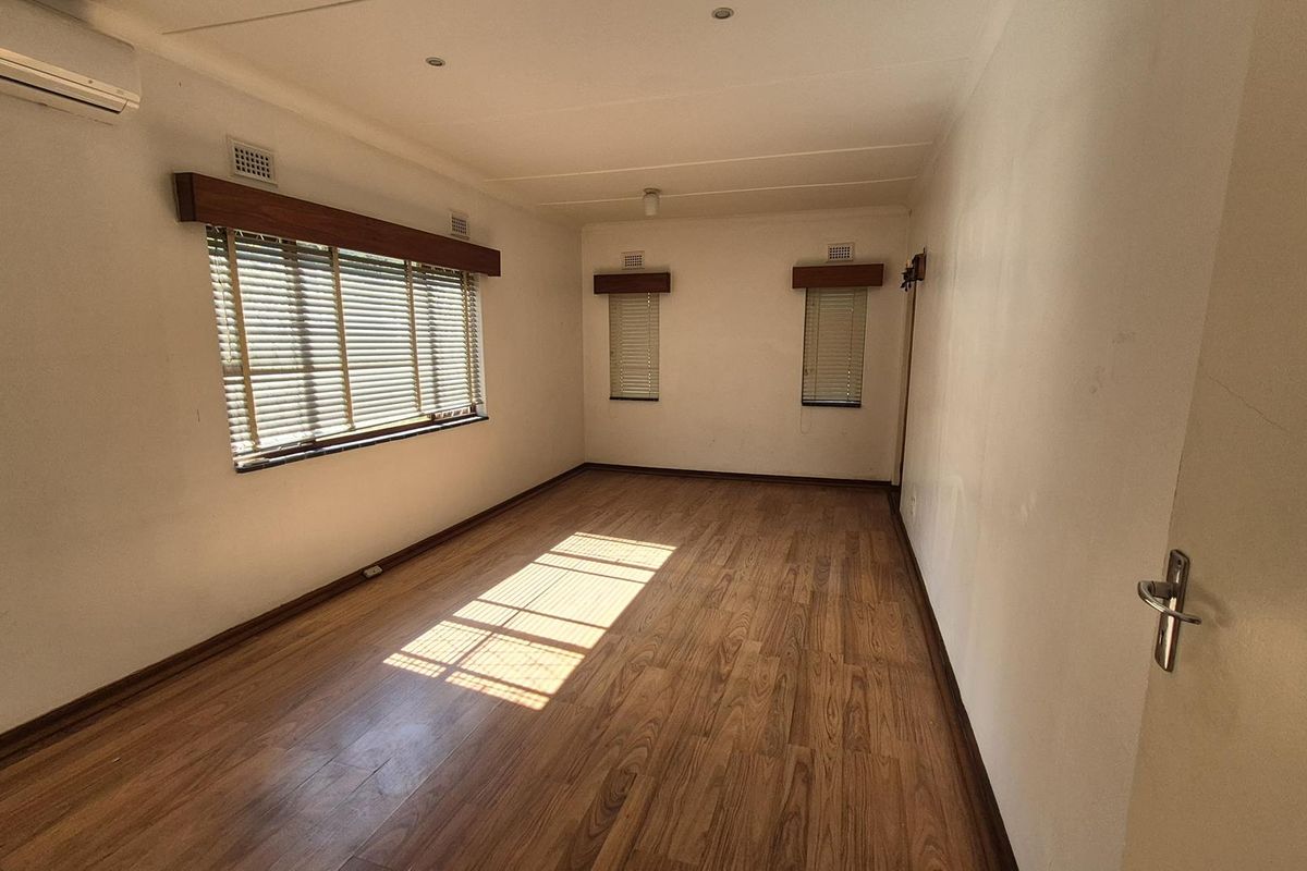 An empty bedroom featuring laminate flooring, venetian blinds, and a wall-mounted air conditioning unit.
