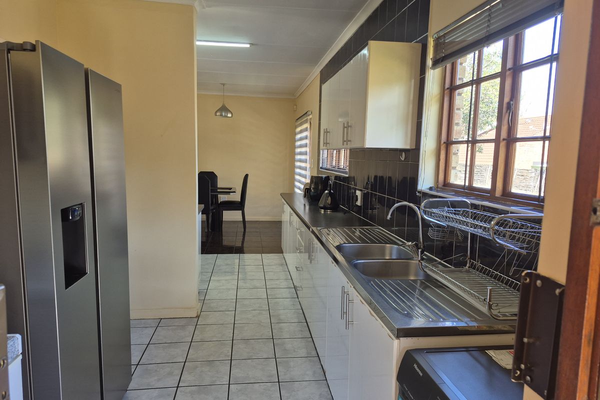 A functional kitchen featuring white cabinetry, a stainless steel double sink, tiled backsplash, and tiled flooring, with an adjacent dining area visible.