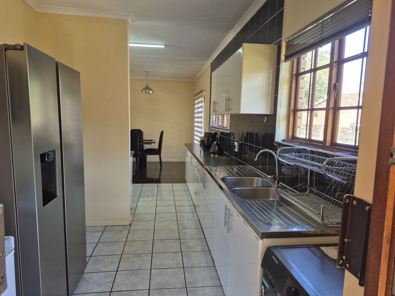 A functional kitchen featuring white cabinetry, a stainless steel double sink, tiled backsplash, and tiled flooring, with an adjacent dining area visible.