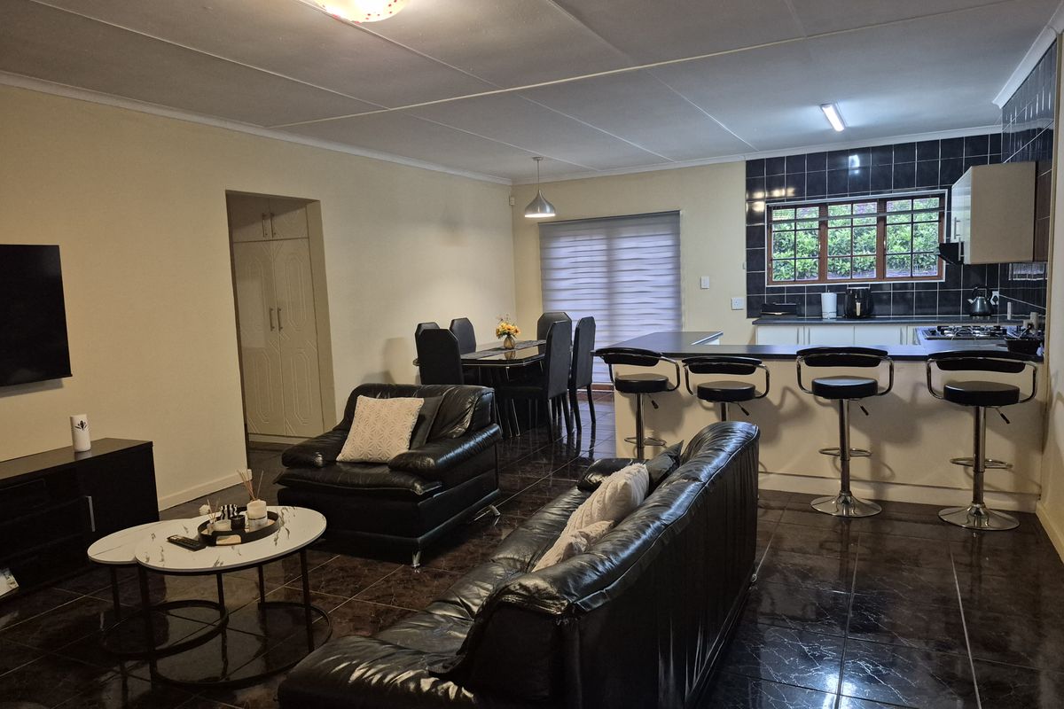 Spacious open-plan living and dining area featuring a modern kitchen with a breakfast bar, dark tiled flooring, and ample built-in cabinetry.