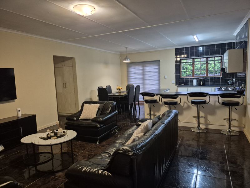 Spacious open-plan living and dining area featuring a modern kitchen with a breakfast bar, dark tiled flooring, and ample built-in cabinetry.