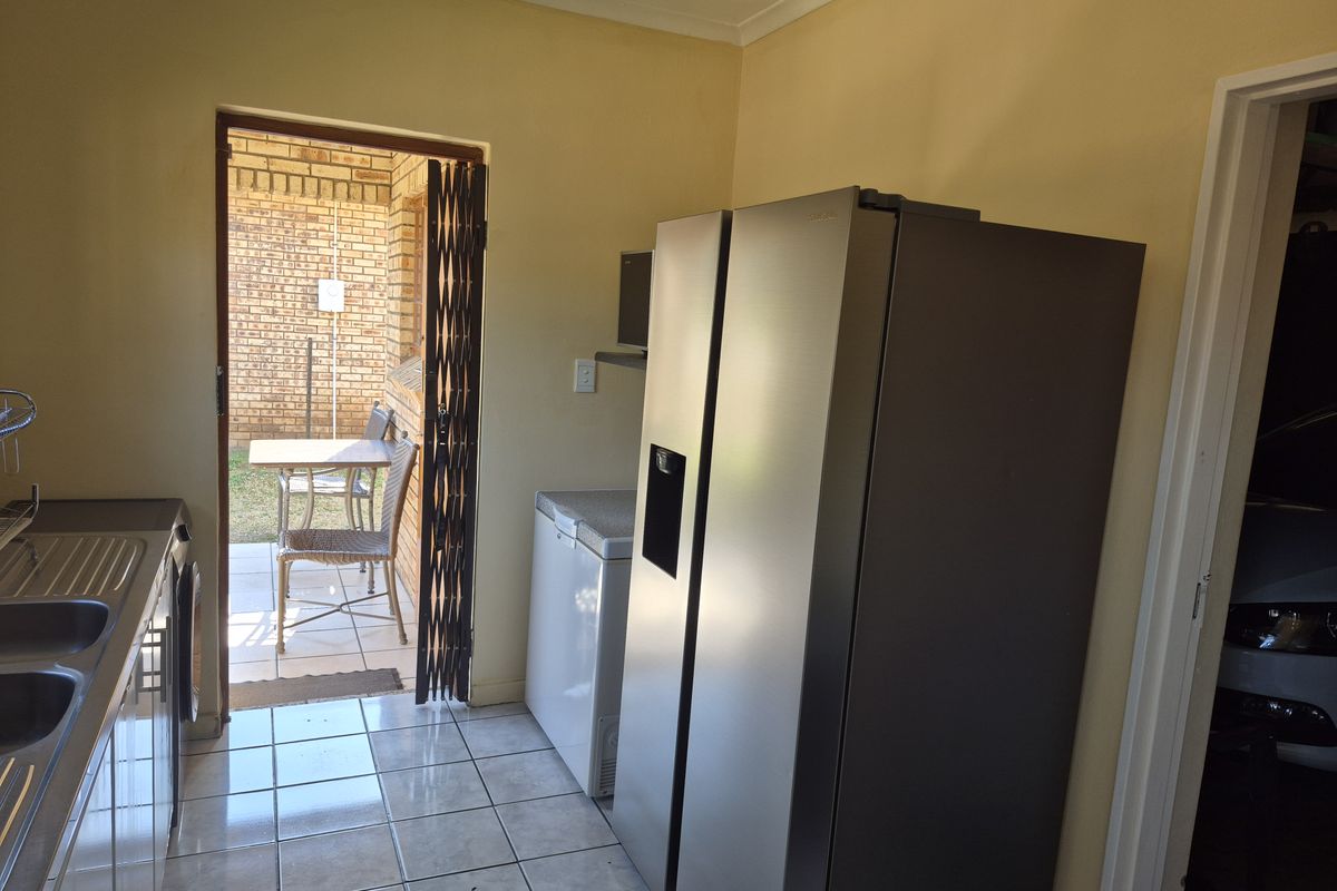 A functional laundry area featuring tiled flooring, a stainless steel sink, and direct access to an outdoor patio space.