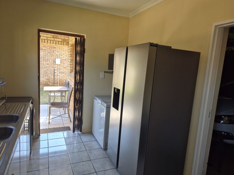A functional laundry area featuring tiled flooring, a stainless steel sink, and direct access to an outdoor patio space.