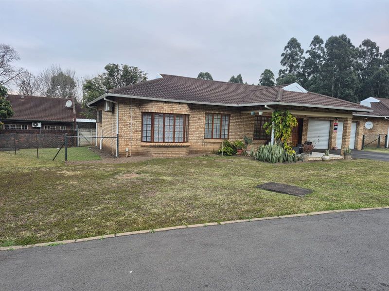Front view of a face-brick townhouse featuring a tiled roof, bay window, and integrated garage, set within a residential complex with a lawn area.