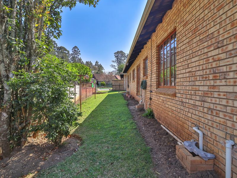 A view of the rear exterior of the townhouse, featuring a face brick facade, timber window frames, and a grass lawn area.