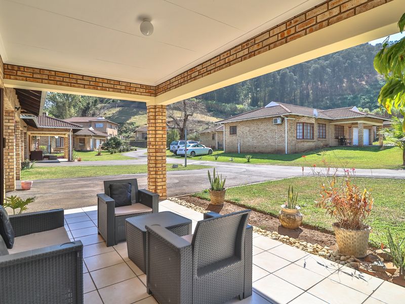 A covered patio area with tiled flooring and brick pillars, overlooking a landscaped residential complex with mountain views.
