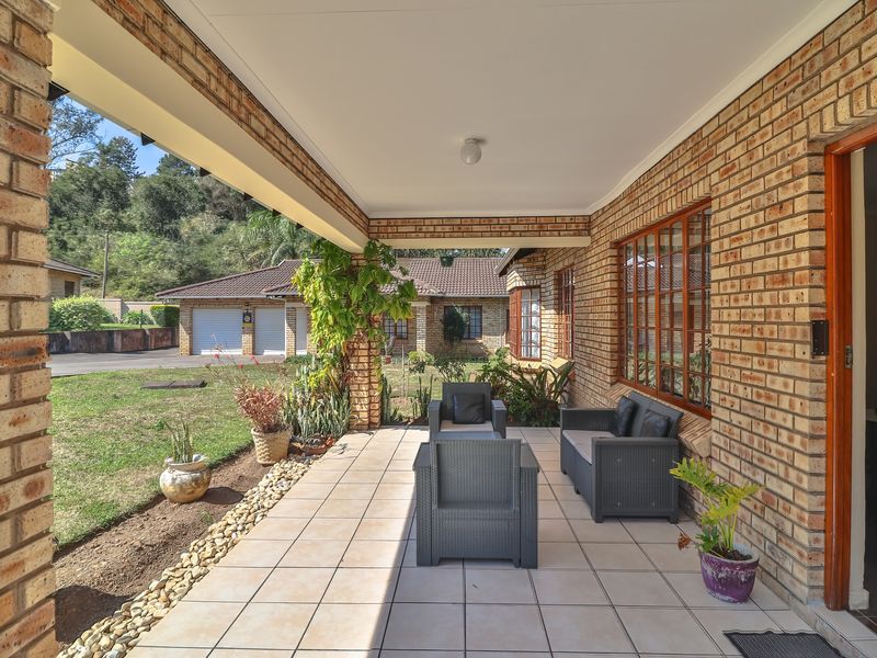 A covered patio area featuring exposed brick walls, tiled flooring, and views overlooking the garden and neighboring properties.