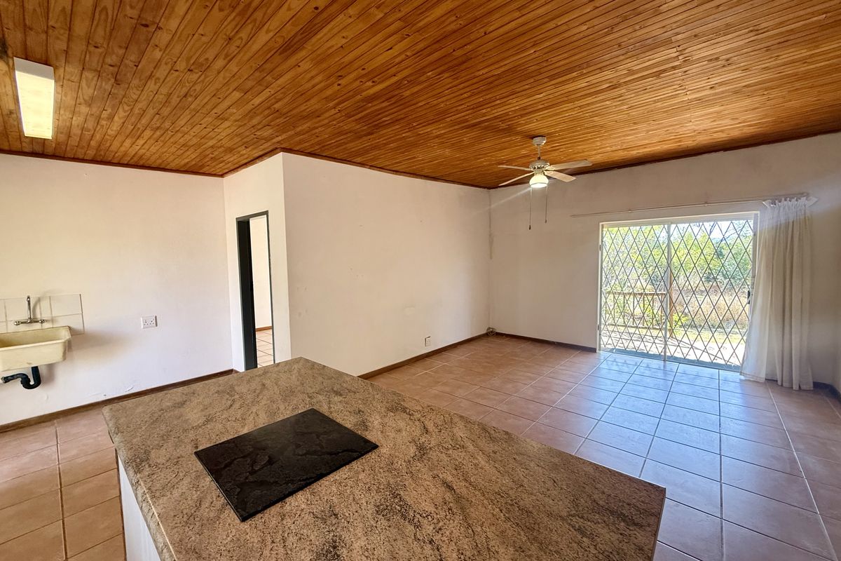 Open-plan living area featuring a timber ceiling, tiled floors, a kitchen island with a built-in hob, and access to an outdoor area via sliding doors.