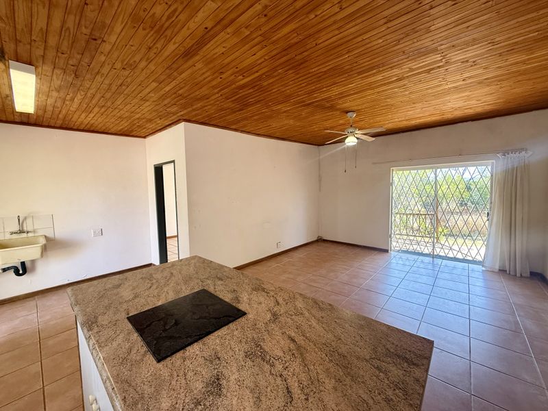 Open-plan living area featuring a timber ceiling, tiled floors, a kitchen island with a built-in hob, and access to an outdoor area via sliding doors.