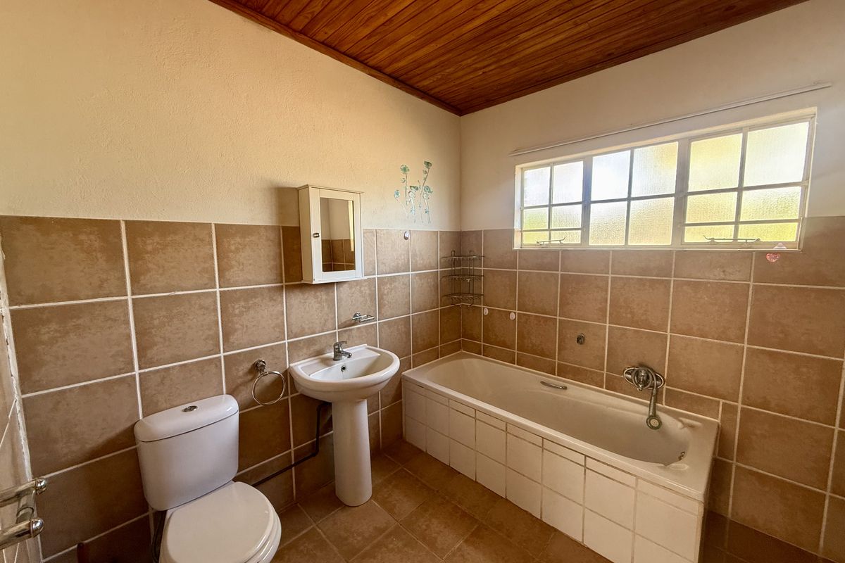 A functional bathroom featuring a pedestal basin, bathtub, toilet, and tiled finishes with a timber ceiling.