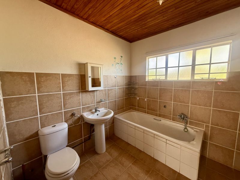 A functional bathroom featuring a pedestal basin, bathtub, toilet, and tiled finishes with a timber ceiling.
