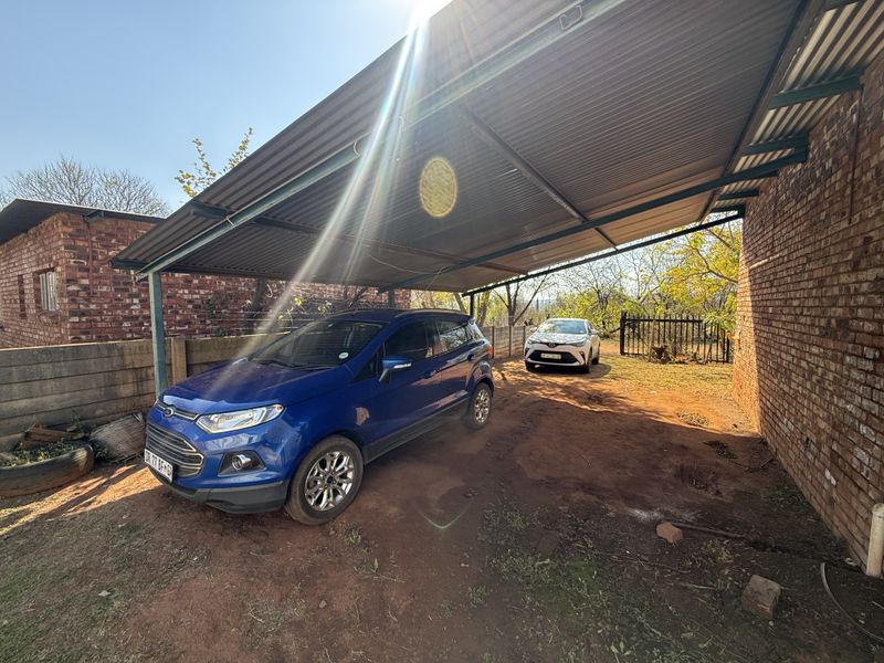 An open-sided carport structure featuring a corrugated metal roof and exposed brick walls, providing covered parking space.