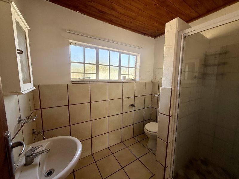 A dated bathroom featuring a shower enclosure, pedestal basin, toilet, tiled surfaces, and a timber ceiling, requiring cosmetic updates.