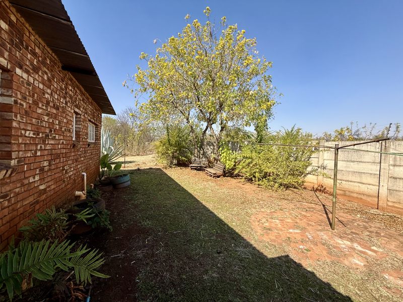 A rear garden area featuring a face brick exterior wall, a precast concrete boundary wall, and a metal washing line set in a lawn area.