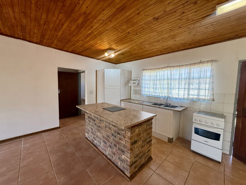 A functional kitchen featuring a brick island with stone countertop, tiled flooring, and a distinctive timber ceiling, offering a dated but practical layout.