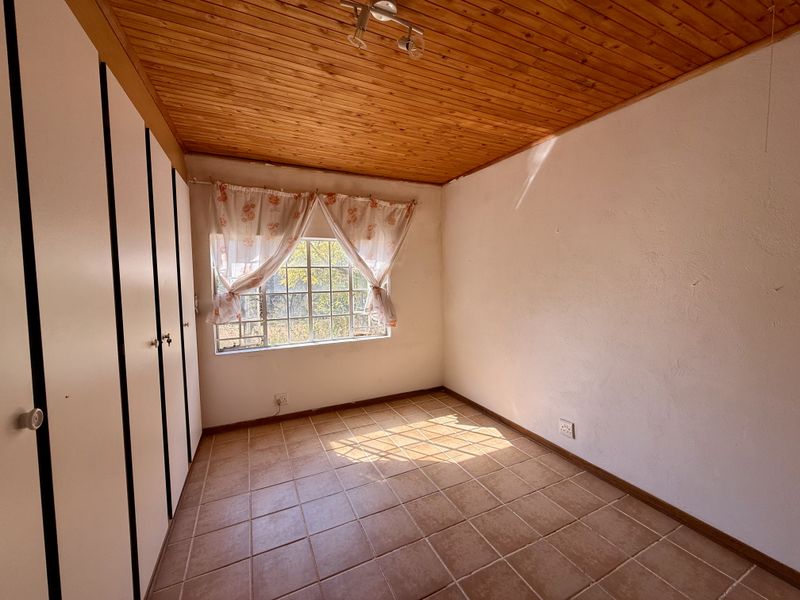 An empty bedroom featuring tiled flooring, built-in cupboards, and a timber-clad ceiling, offering a blank canvas for potential renovation or staging.