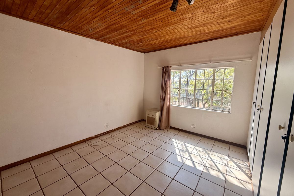An empty bedroom featuring tiled flooring, built-in cupboards, and a timber-clad ceiling, offering a blank canvas for renovation.