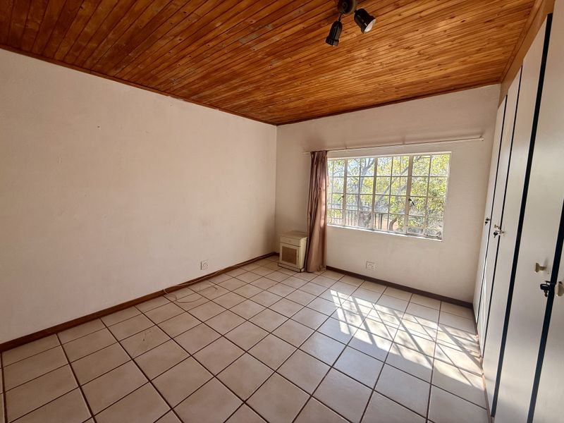 An empty bedroom featuring tiled flooring, built-in cupboards, and a timber-clad ceiling, offering a blank canvas for renovation.