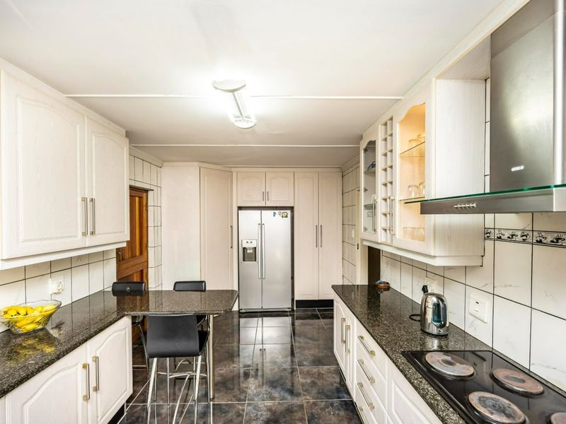 A well-maintained kitchen featuring granite countertops, ample built-in cabinetry, an electric hob with extractor fan, and polished tiled flooring.
