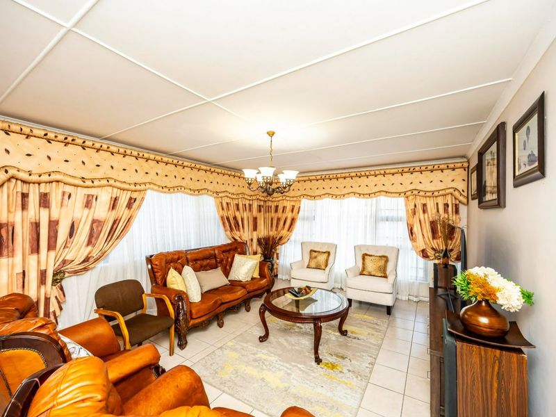 A spacious living room featuring tiled flooring, a central chandelier, and large windows with decorative pelmets.