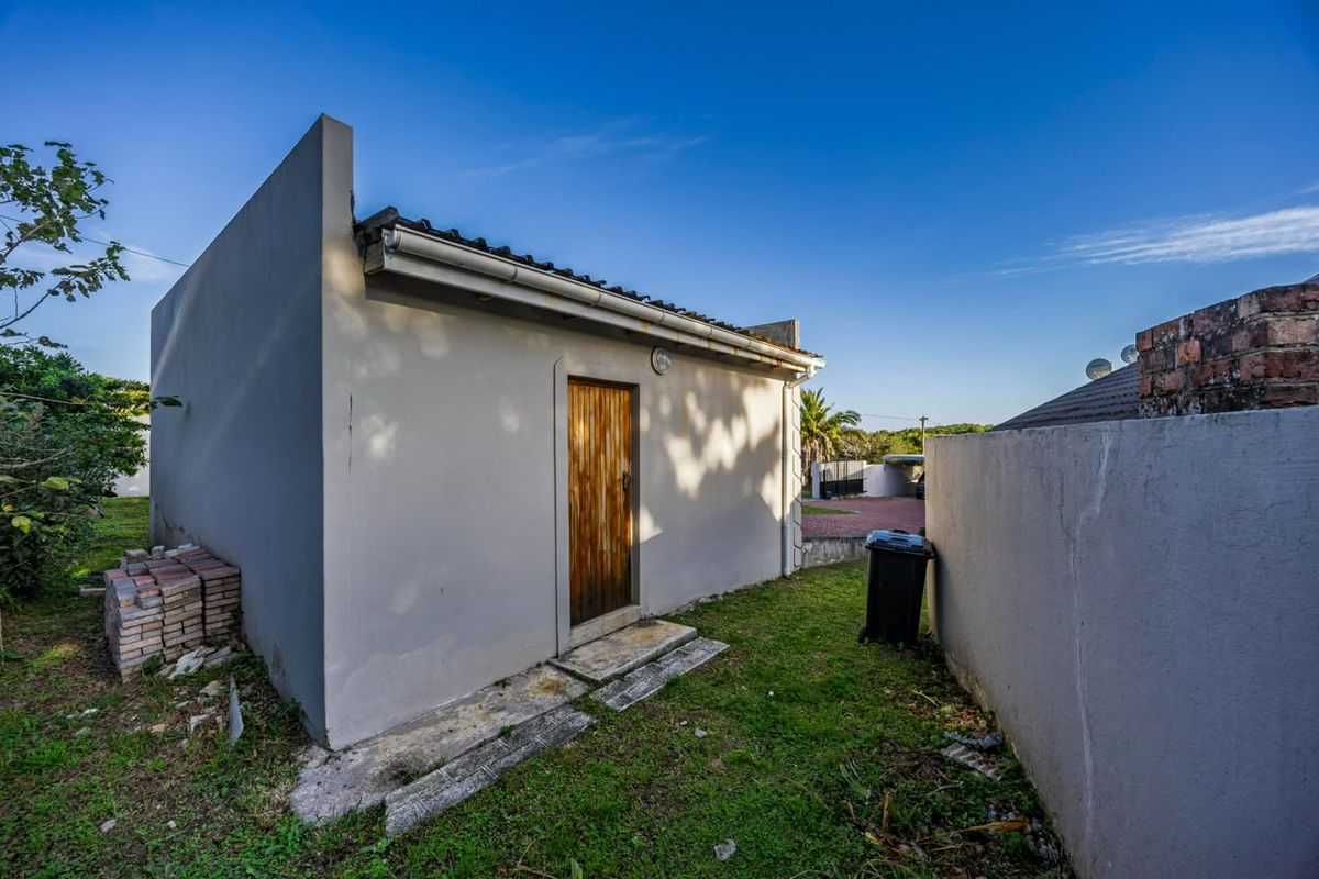 Rear exterior view of a small outbuilding featuring a timber door, guttering, and a concrete pathway set within a garden area.