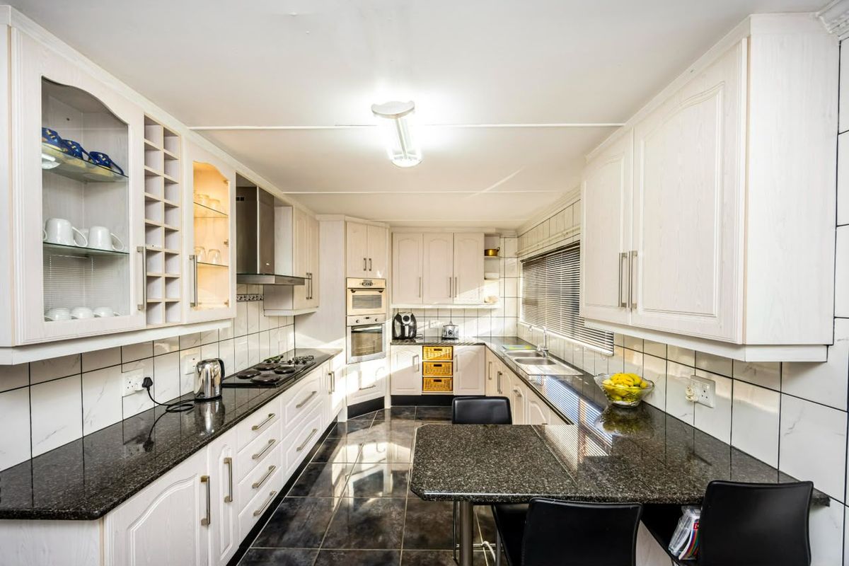 A functional kitchen featuring granite countertops, built-in oven, gas hob, extractor fan, and ample cabinetry with a tiled splashback and floor.