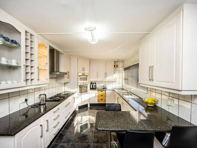 A functional kitchen featuring granite countertops, built-in oven, gas hob, extractor fan, and ample cabinetry with a tiled splashback and floor.