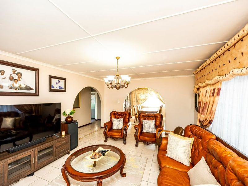 A spacious living room featuring tiled flooring, arched architectural transitions to adjacent rooms, and a central chandelier, offering a traditional layout.
