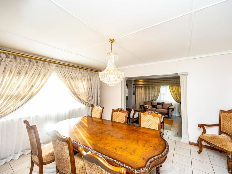 A formal dining room featuring tiled flooring, a classic crystal chandelier, and an open archway leading into an adjacent living area.