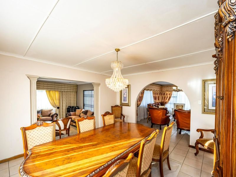 Open-plan dining and living area featuring tiled floors, decorative archways, classic columns, and a central crystal chandelier.