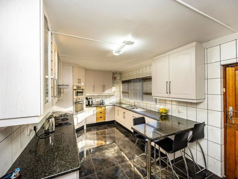 A functional kitchen featuring granite countertops, built-in cabinetry, integrated oven and hob, and tiled finishes throughout.