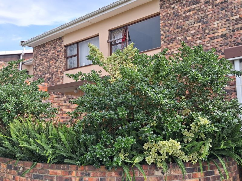 A view of the townhouse exterior featuring a face brick facade, established garden landscaping, and a low brick retaining wall.