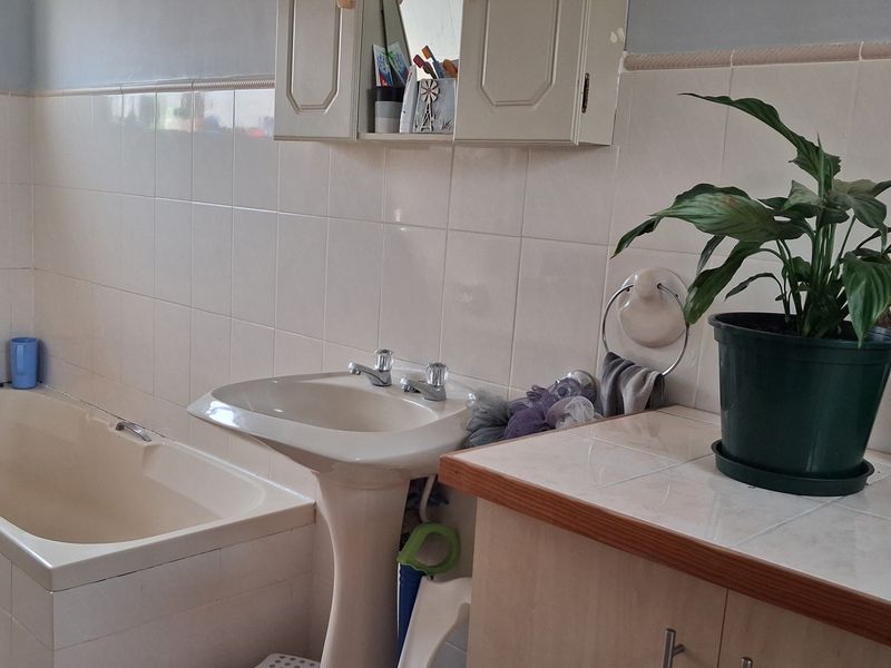 A functional bathroom featuring a built-in bathtub, pedestal washbasin, and tiled vanity area with wall-mounted storage cabinet.