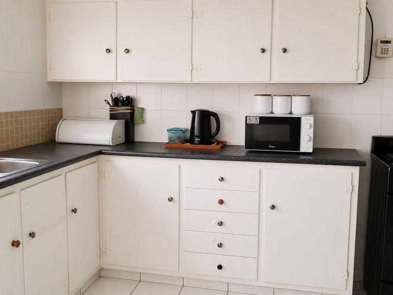A functional kitchen featuring white cabinetry, dark laminate countertops, a double sink, and a tiled backsplash with a freestanding stove.