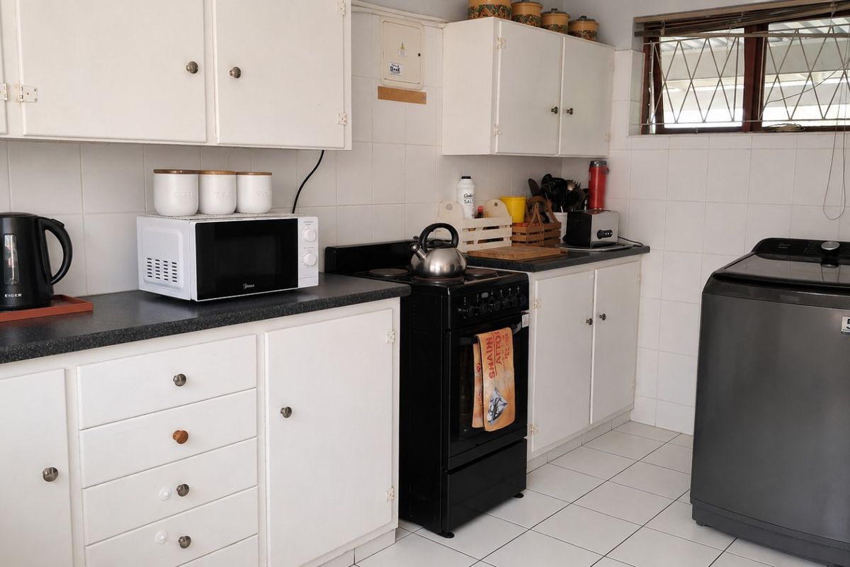 A functional kitchen featuring white cabinetry, dark laminate countertops, a freestanding stove, and tiled surfaces throughout.