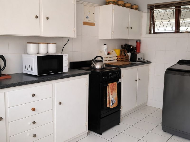 A functional kitchen featuring white cabinetry, dark laminate countertops, a freestanding stove, and tiled surfaces throughout.