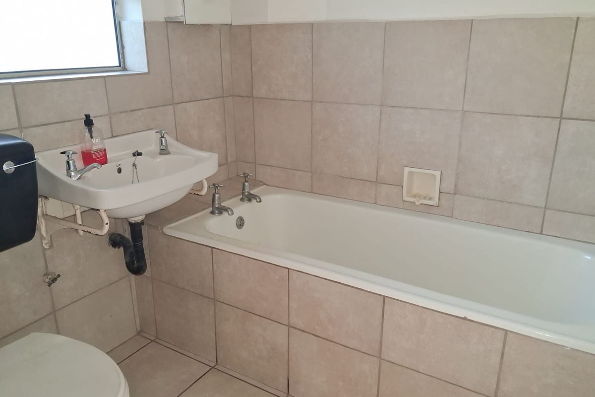A functional bathroom featuring a built-in bathtub, wall-mounted basin, and neutral ceramic tiling throughout.