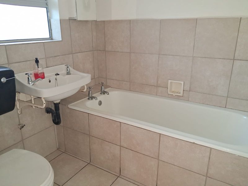 A functional bathroom featuring a built-in bathtub, wall-mounted basin, and neutral ceramic tiling throughout.