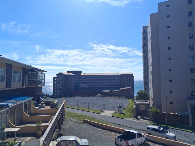 An elevated view overlooking a residential complex, paved driveway, and surrounding apartment buildings with a distant ocean horizon.